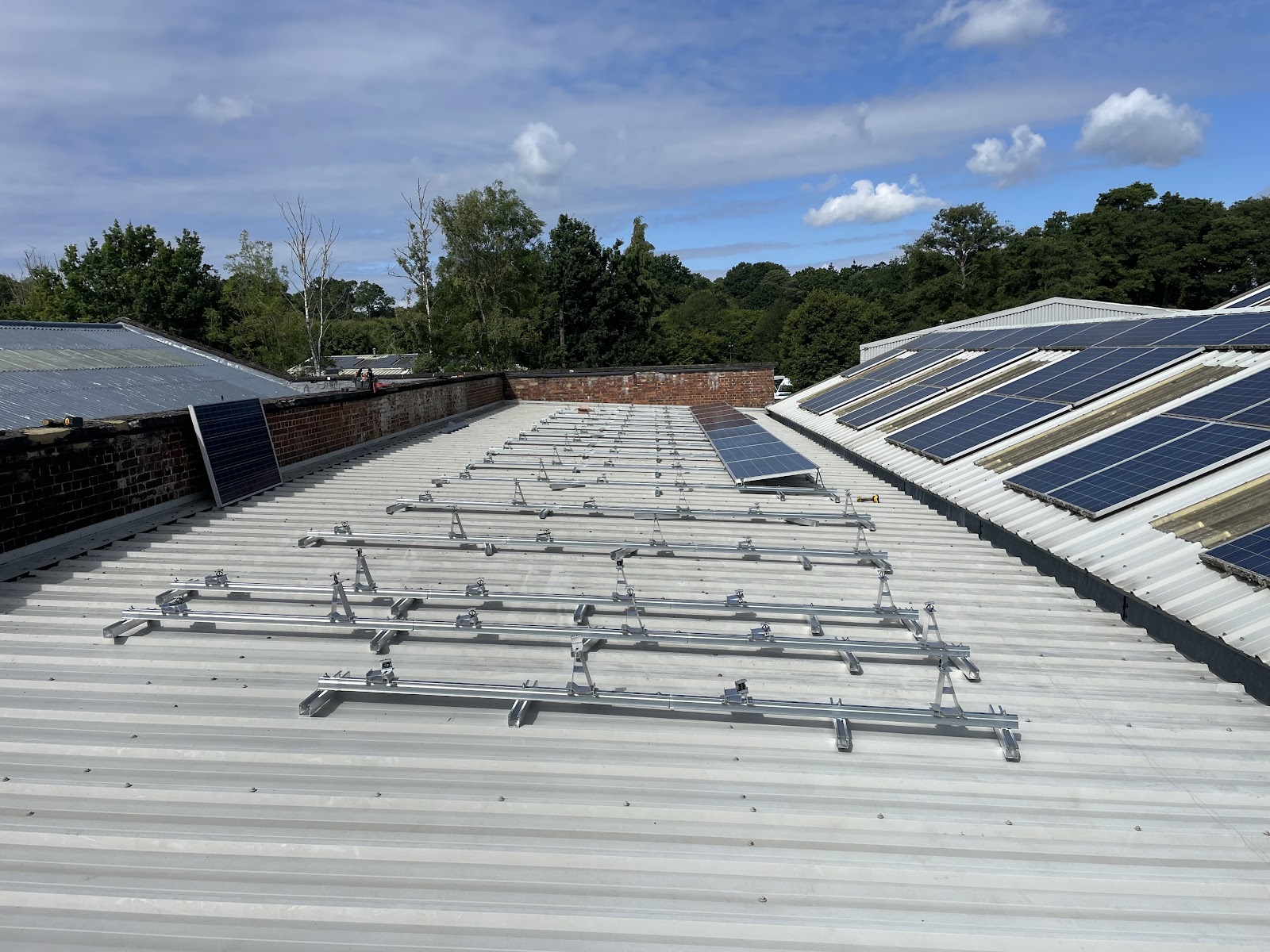 Mounting rails laid out on a commercial metal roof, with a finished solar array beyond