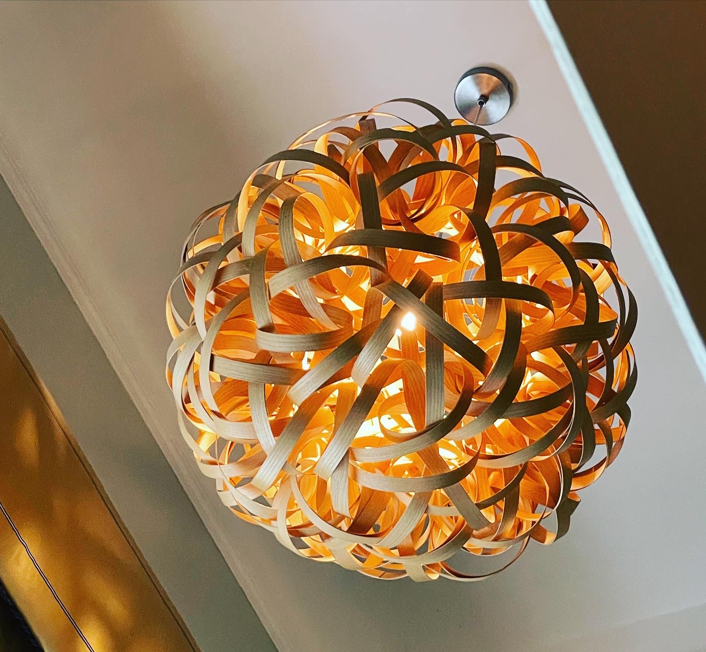 A woven copper and timber pendant light, lit