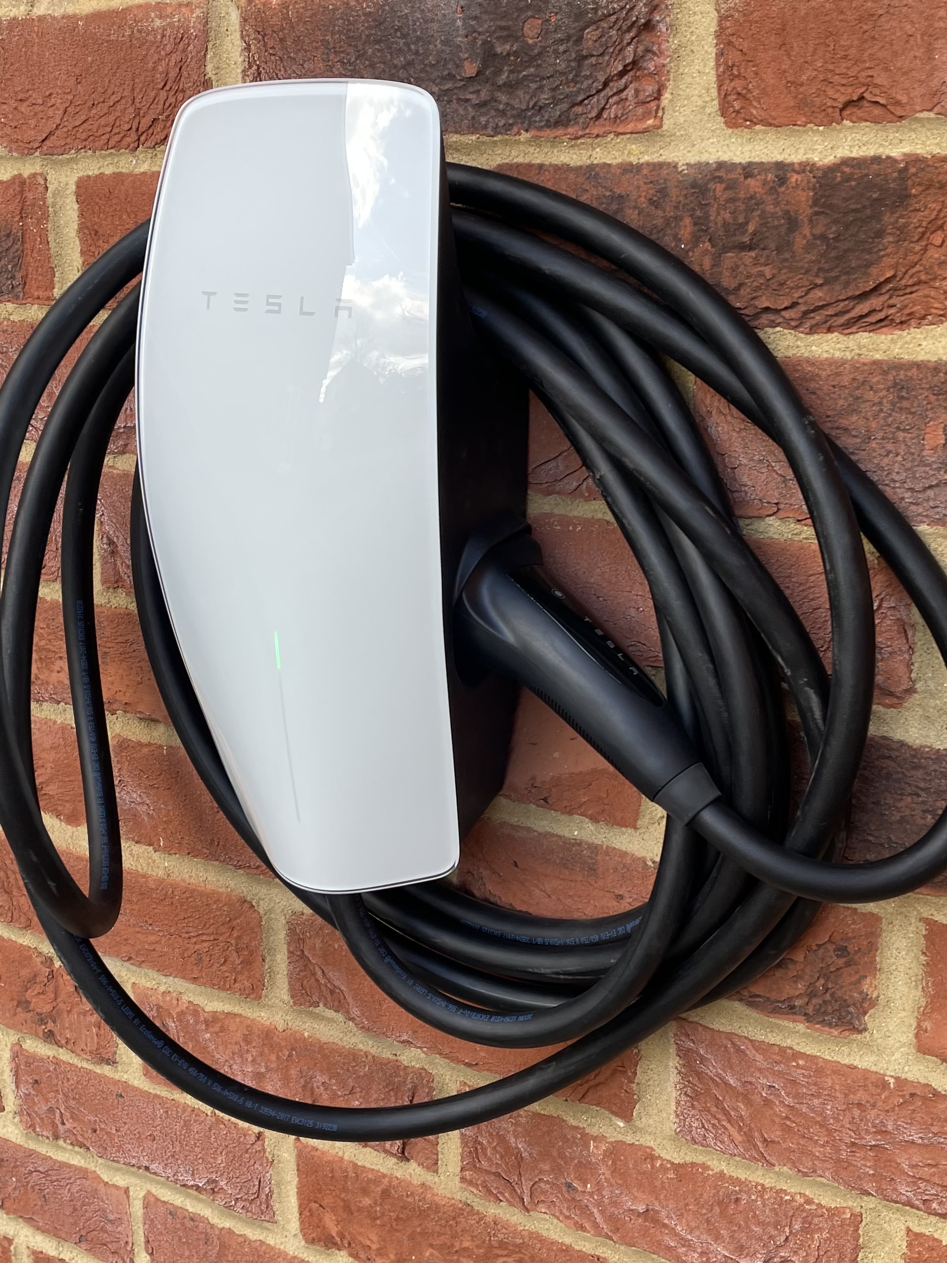 A white wall charger with its cable coiled, on a brick wall